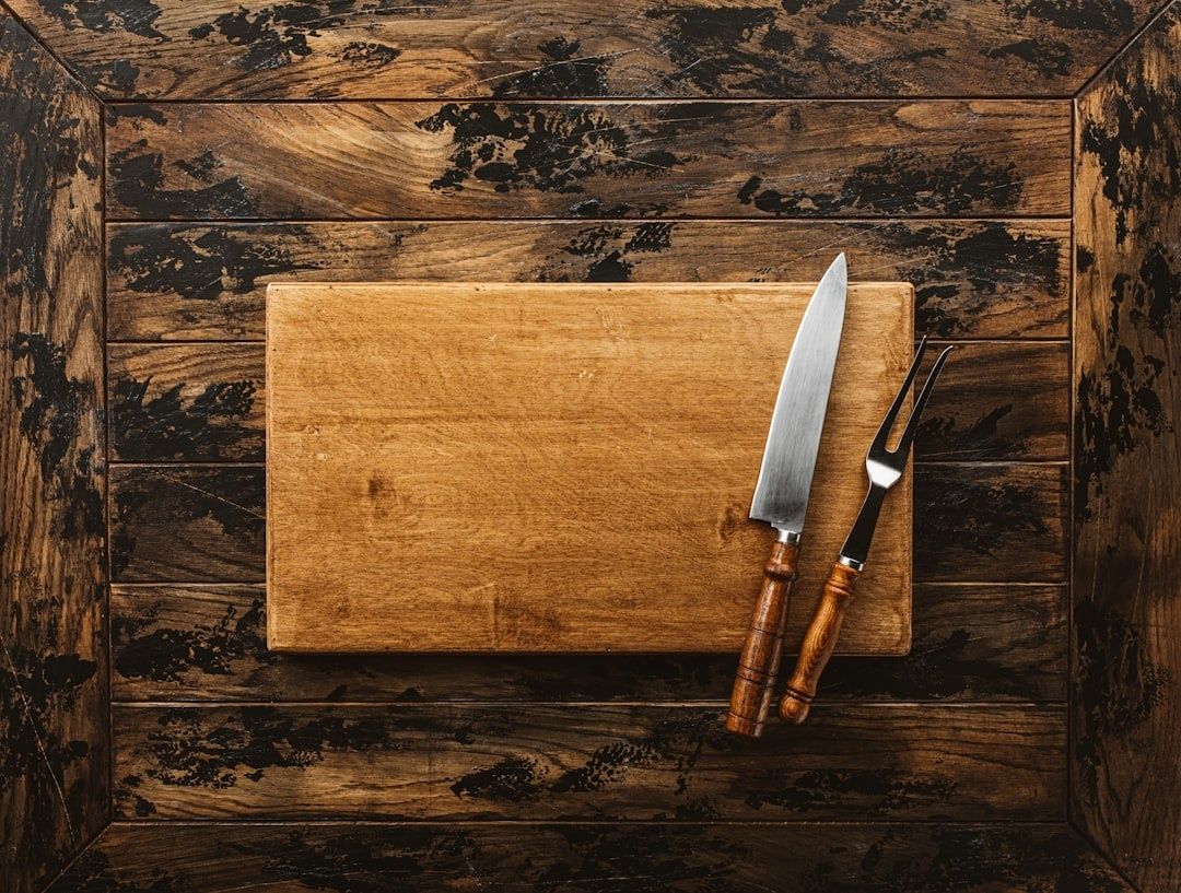 Treskjærebrett med kokkekniv og gaffel på rustikk treflate